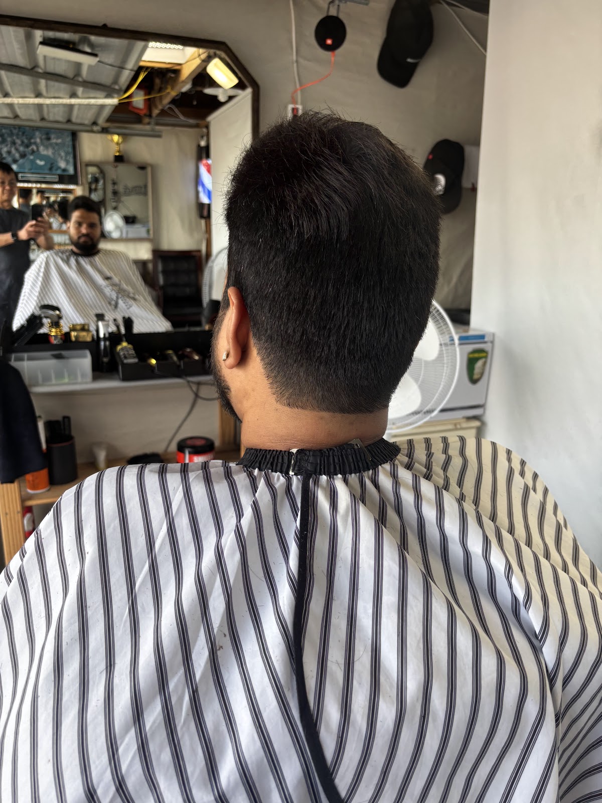 Manny at work behind the chair, seen in the shop mirror